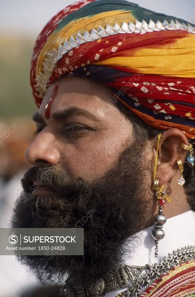 India, Rajasthan, Jaisalmer, Head And Shoulders Side Profile Portrait Of A Mr Desert Contestant With A Beard Wearing A Colourful Turban And Traditional Earrings At The Desert Festival