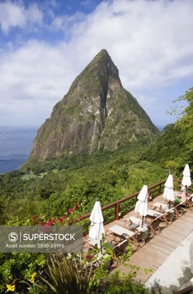 West Indies, St Lucia, Soufriere , Val Des Pitons The Volcanic Plug Of Petit Piton And The Lush Valley Seen From The Sun Deck Of The Ladera Spa Resort Hotel With Tourists Sunbathing On Sunbeds Beside Umbrellas