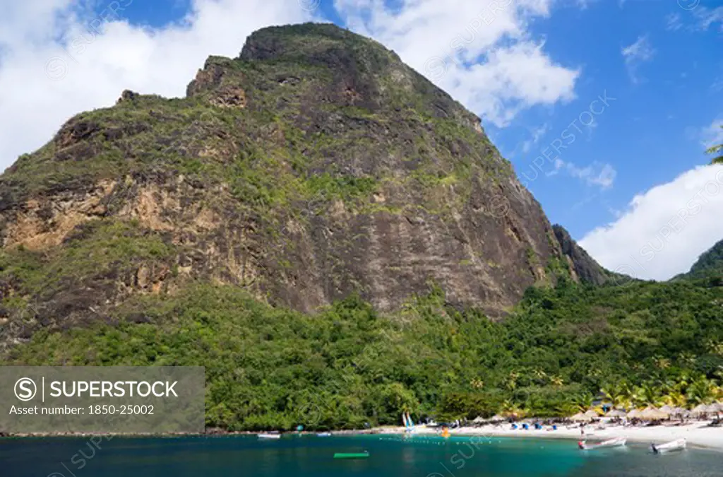 West Indies, St Lucia, Soufriere , Val Des Pitons The White Sand Beach At The Jalousie Plantation Resort Hotel With The Volcanic Plug Of Petit Piton Beyond And Tourists On Sunbeds Beneath Palapa Sun Shades