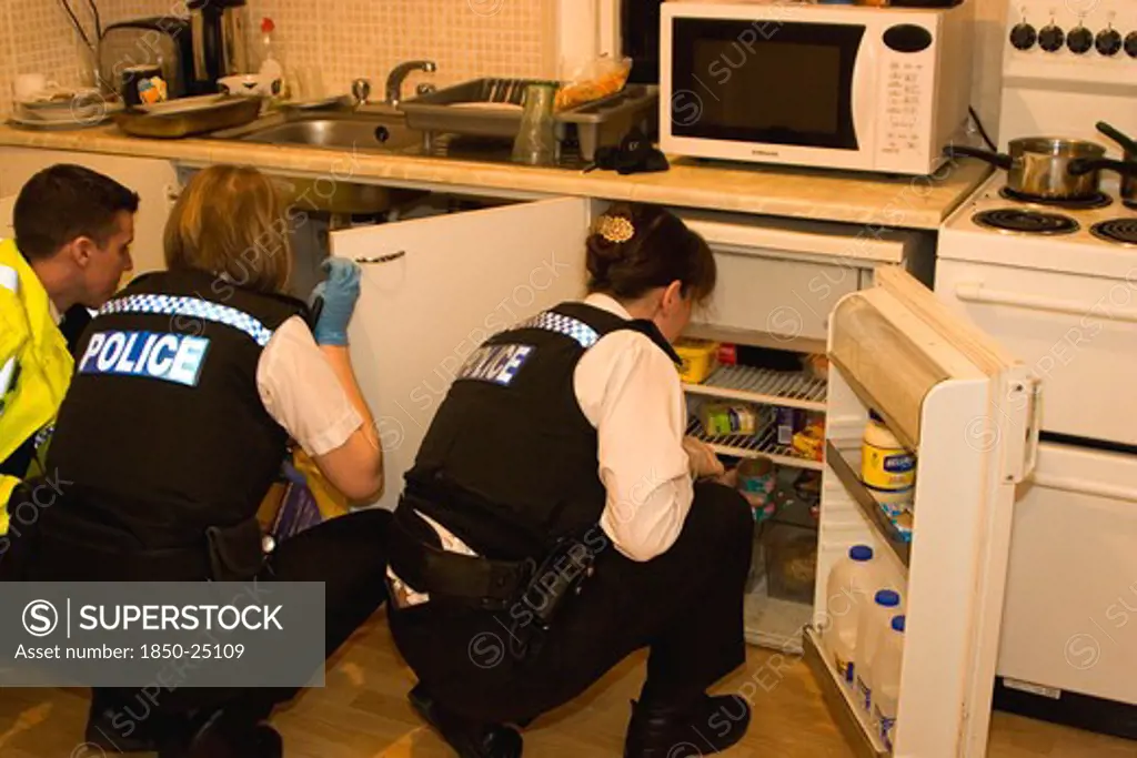 Law And Order, Police, Drugs Raid, Police Searching Kitchen Of Residential Home During Drugs Bust.