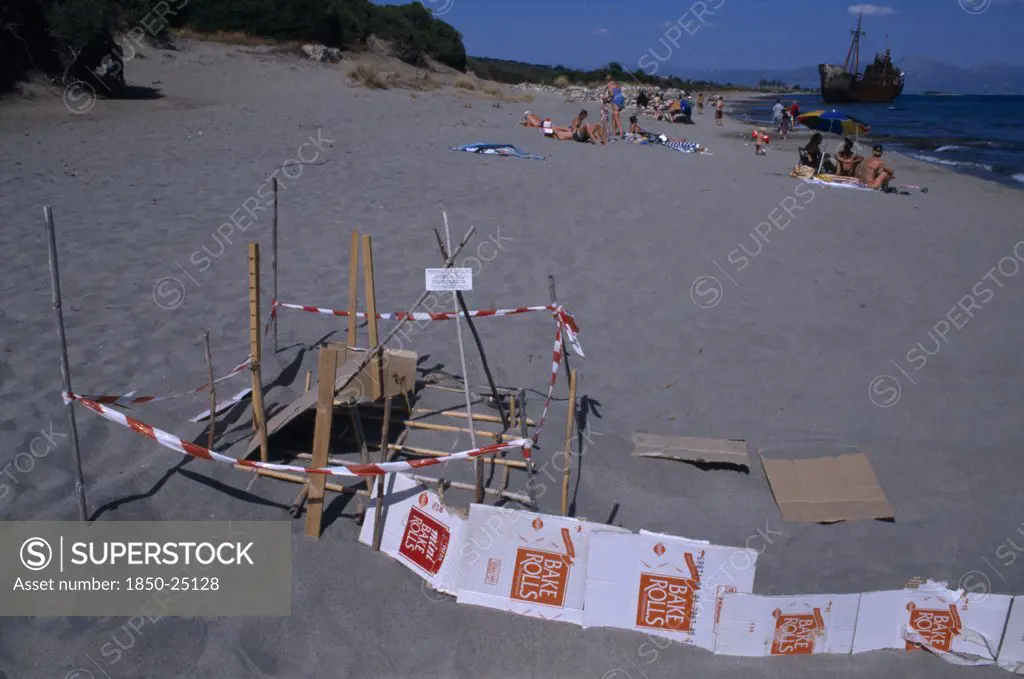 Greece, Peloponnese, Sea Turtle Protection Consisting Of Wood And Cardboard Forming A Cordon Around An Area On Sandy Beach Near Sunbathers