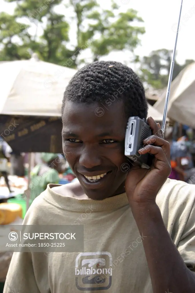 Gambia, Atlantic Coast, Banjul, 'Albert Market, Russell Street.  Young African Man Smiling  While Listening To A Radio Which He Is Holding Next To His Ear.'