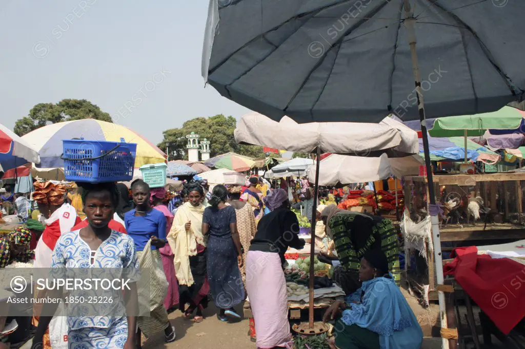 Gambia, Western Gambia, Serekunda, 'Bakau Market, Atlantic Road.  Busy Market Scene With Women Selling Fruit And Vegetables.  Woman In Foreground Carrying Box On Her Head.'