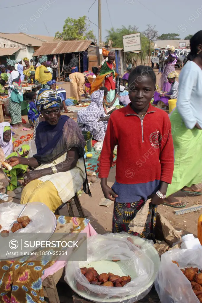 Gambia, Western Gambia, Tanji, Tanji Market.  Young Girl Selling Sweet Snacks At Tanji Market With Older Woman Seated At Stall Beside Her.