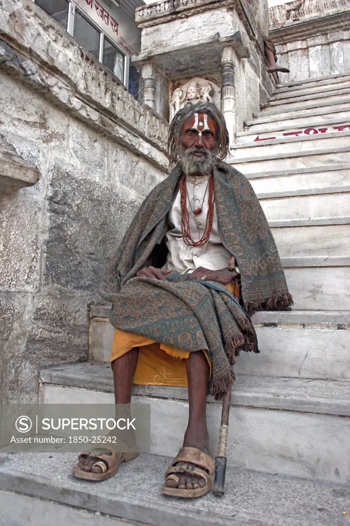 India, Rajasthan, Udaipur, Elderly Male Hindu Beggar Sitting On Steps Outside The Jagdish Temple Wrapped In Blanket Shawl With Painted Forehead And Grey Beard.