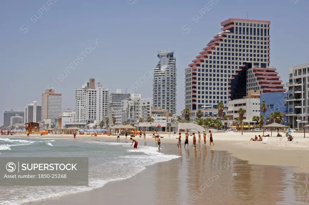 Israel, Tel Aviv, 'Beach With People Sunbathing And At Waters Edge Overlooked By High Rise, Modern City Buildings Reflected On Wet Sand.'