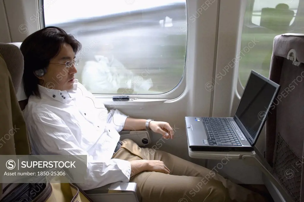 Japan, Honshu, Shinkansen Train Series 700 Known As The Bullet Train.  Young Japanese Man Using His Laptop With A Wireless Connection While Travelling Between Tokyo And Kyoto.