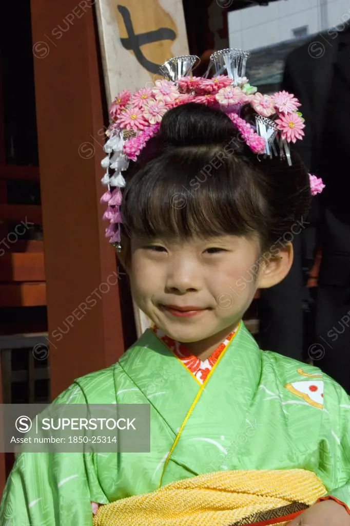 Japan, Honshu, Tokyo, Asakusa Kannon Or Senso-Ji Temple.  Head And Shoulders Portrait Of Young Japanese Girl Wearing Pink Flower Decoration In Her Hair And Green Kimono.
