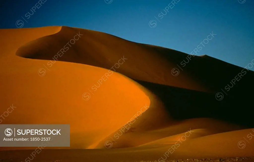 Libya , Achan, Sand Dune Partially Cast In Shadow Against Blue Sky