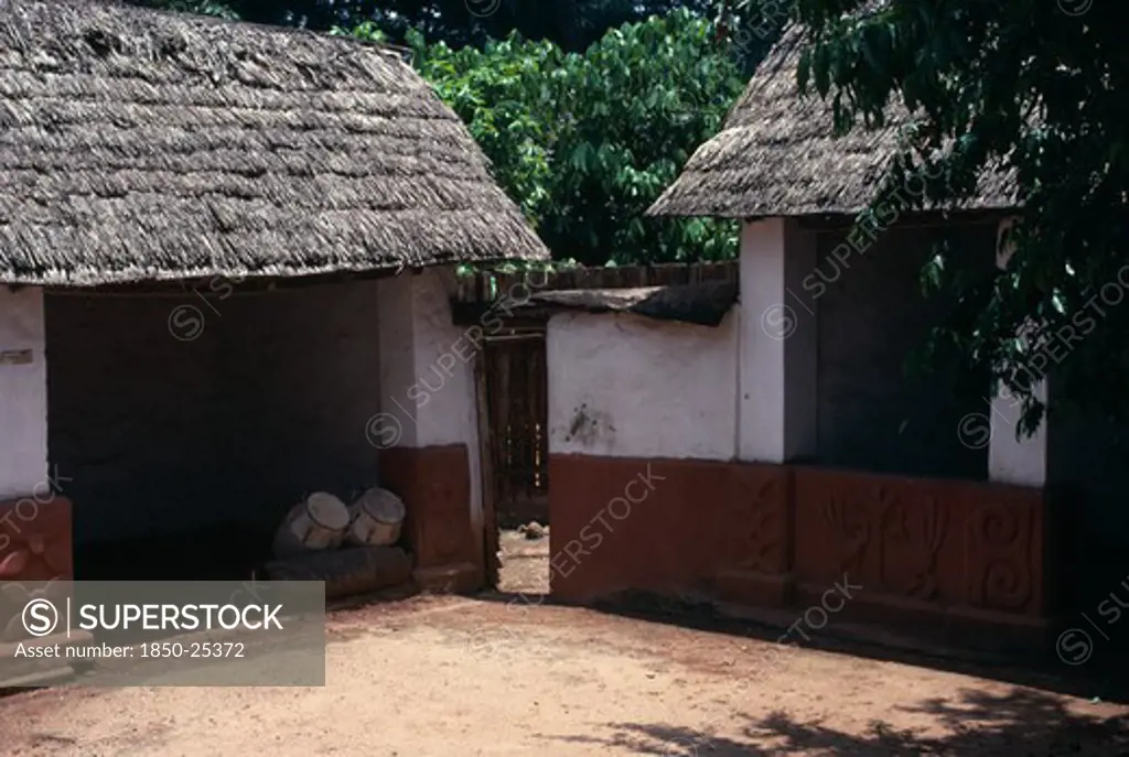 Ghana, Ashanti, Traditional Thatched House With Intricate Patterns On Walls. Ceremonial Drums Inside One Of The Huts.