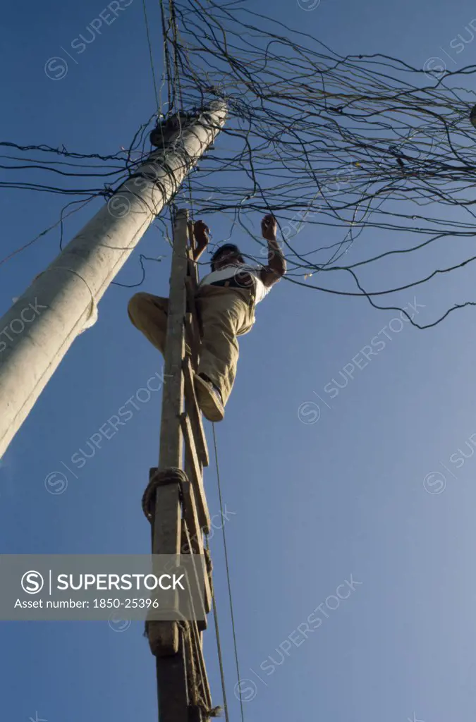 Ecuador, Guayas Province, Guayaquil , Barrio Indio Guayas Slum Neighbourhood. Man On Ladder Illegally Connecting Into The Overhead Mains Electricity Supply.