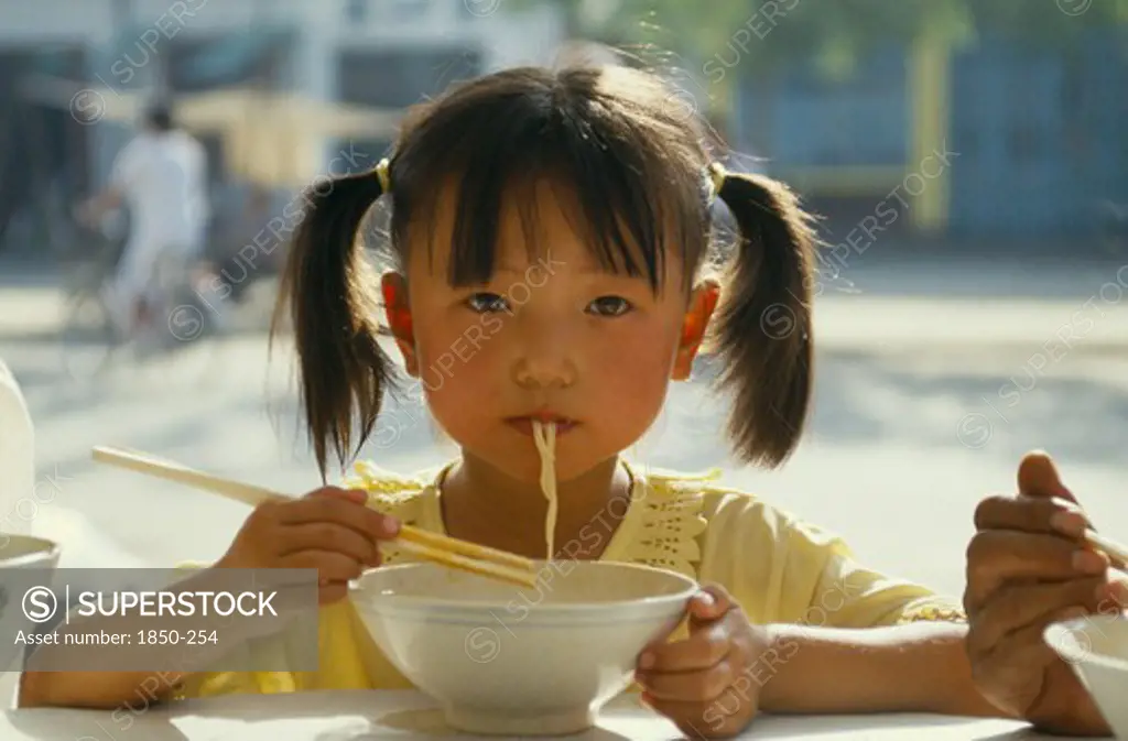 China, Guizhou, Guiyang, Pony Tailed Young Girl Eating Noodles From Bowl With Chopsticks