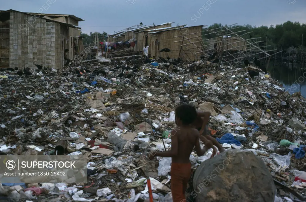 Ecuador, Guayas Province, Guayaquil , The City Rubbish Tip In Barrio Guayas Slum Neigbourhood With Children Playing Near Large Rock In The Foreground.