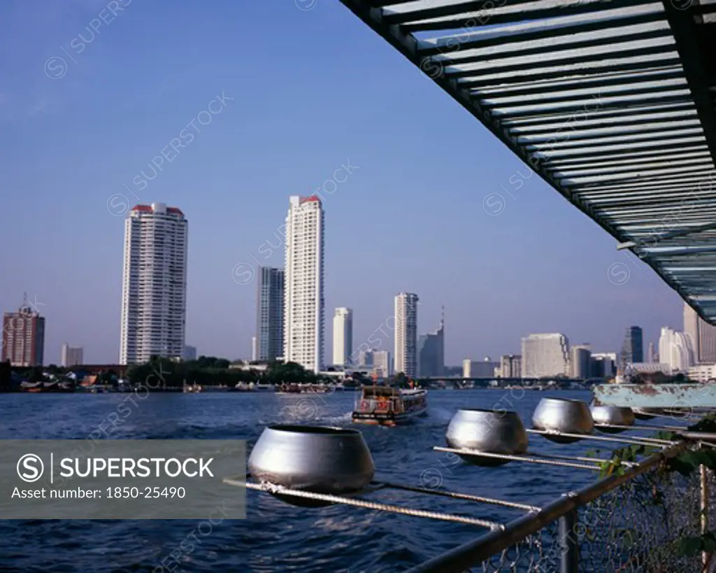 Thailand, Bangkok, 'Chao Phraya River From Wat Ratchasungkhon Decorated With Silver Alms Bowls, High Rise Buildings On Opposite Bank Including Shangri-La Hotel And New Apartments With River Ferry Departing North For Saphan Thaksin Bridge Stop.'