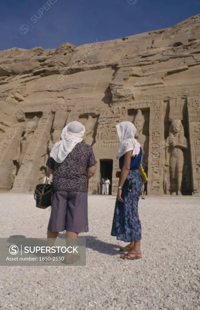 Egypt, Abu Simnel , Two Female Tourists Wearing Head Scarves In Front Of Staues Of Ramesses Ii At The Temple Entrance
