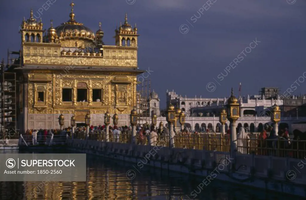India, Punjab, Amritsar, The Sikh Golden Temple With People On The Walkway Across The Water