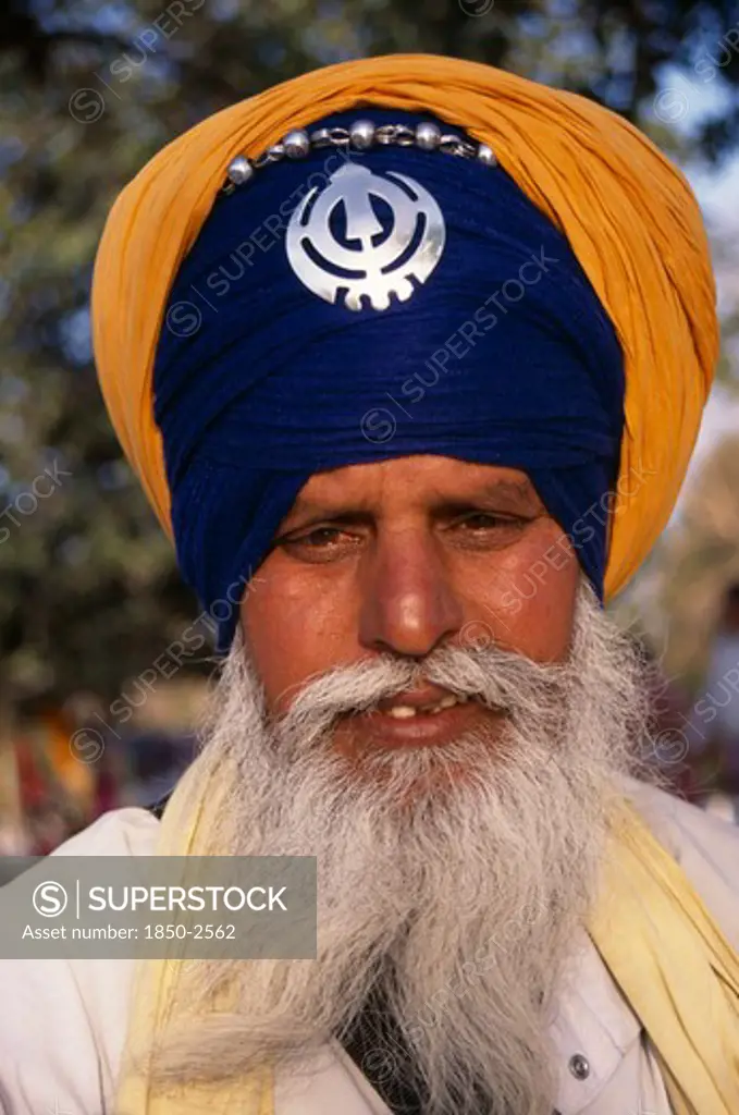 India, Delhi, 'Portrait Of A Sikh Man Wearing Orange And Royal Blue  Turban Set With A Khanda, The Symbol Of Sikhdom And With Grey Beard And Moustache.'