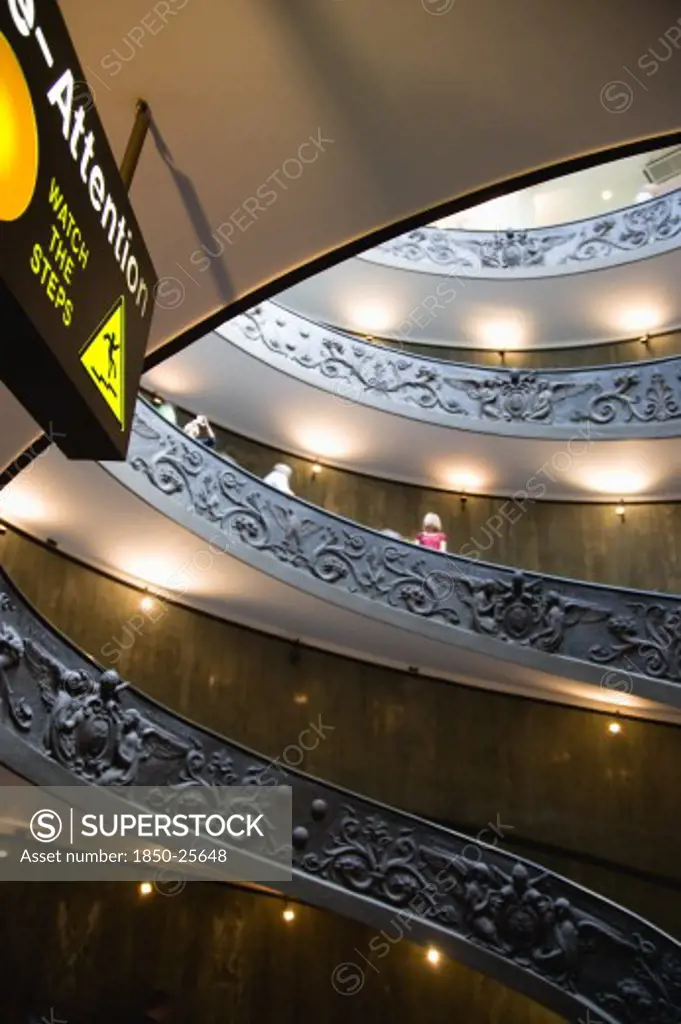 Italy, Lazio, Rome, Vatican City Museums Tourists Descending The Spiral Ramp Designed By Giuseppe Momo In 1932 Leading From The Museums To The Street Level Below Seen From Below With An Illuminated Sign Warning To Watch The Steps