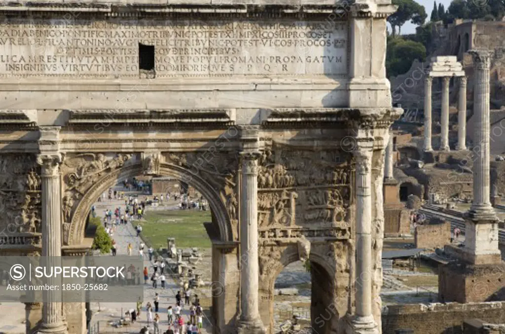 Italy, Lazio, Rome, The Forum With The Triumphal Arch Of Septimus Severus In The Foreground And The Three Corinthian Columns Of The Temple Of Castor And Pollux In The Distance With Tourists Walking Around