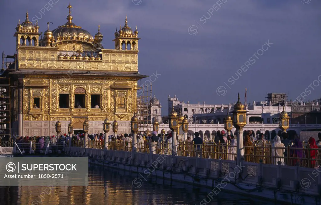 India, Punjab, Amritsar, Pilgrims On Causeway Known As The GuruS Bridge Leading To The Golden Temple Reflected In Rippled Surface Of Pool Below.