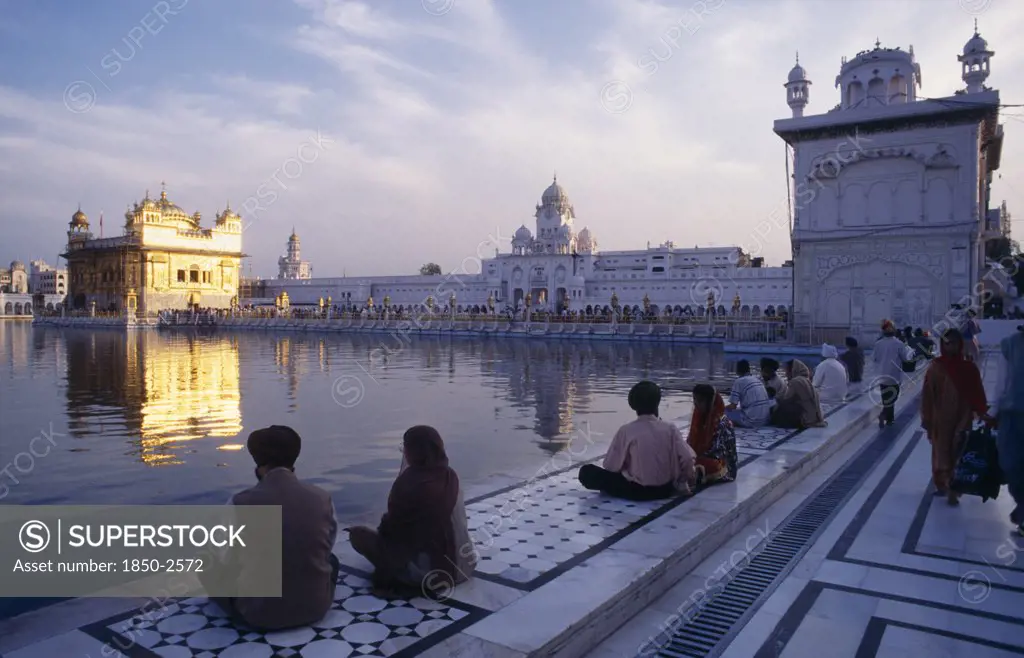 India, Punjab, Amritsar, Golden Temple With Pilgrims In Low Light With Shimmering Temple Reflected In Water Of Sacred Pool.