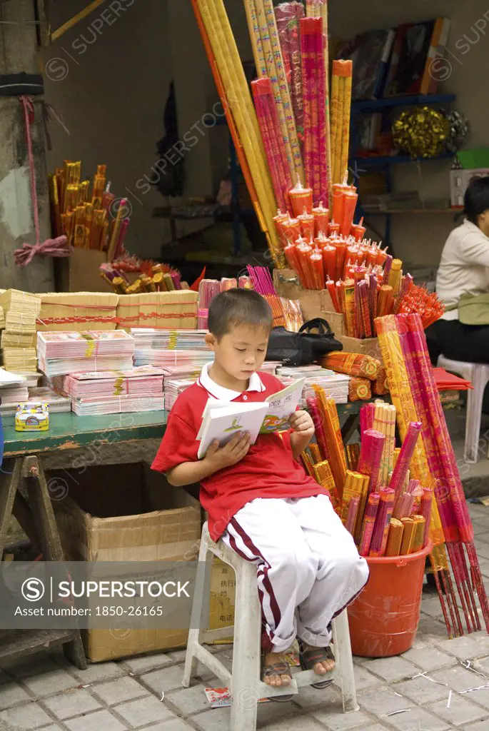 China, Sichuan Province, Chongqing, Boy Incense Seller Reading Book Outside The Arhat Temple In Downtown Chongqing