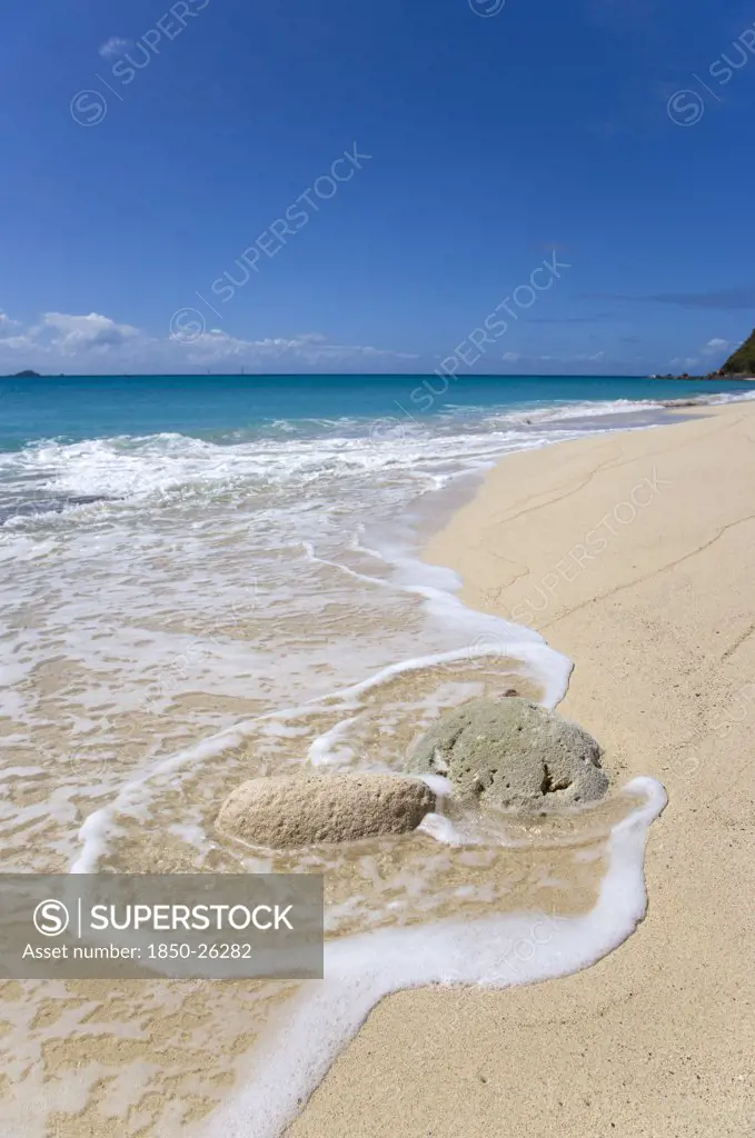 West Indies, St Vincent And The Grenadines, Canouan Island, South Glossy Beach In Glossy Bay With Waves Breaking Around A Large Piece Of Coral On The Shoreline Of The Turqoise Sea.