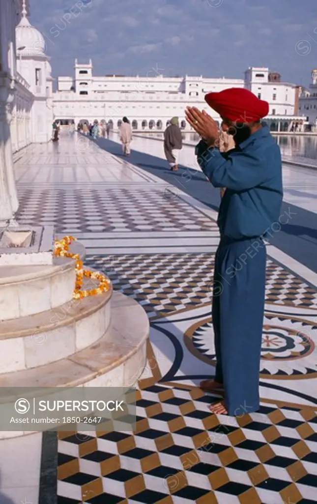 India, Punjab, Amritsar, Golden Temple.  Barefooted Sikh Man Praying In Front Of Shrine With Garland Of Marigold Flowers Lying Across Marble Steps.