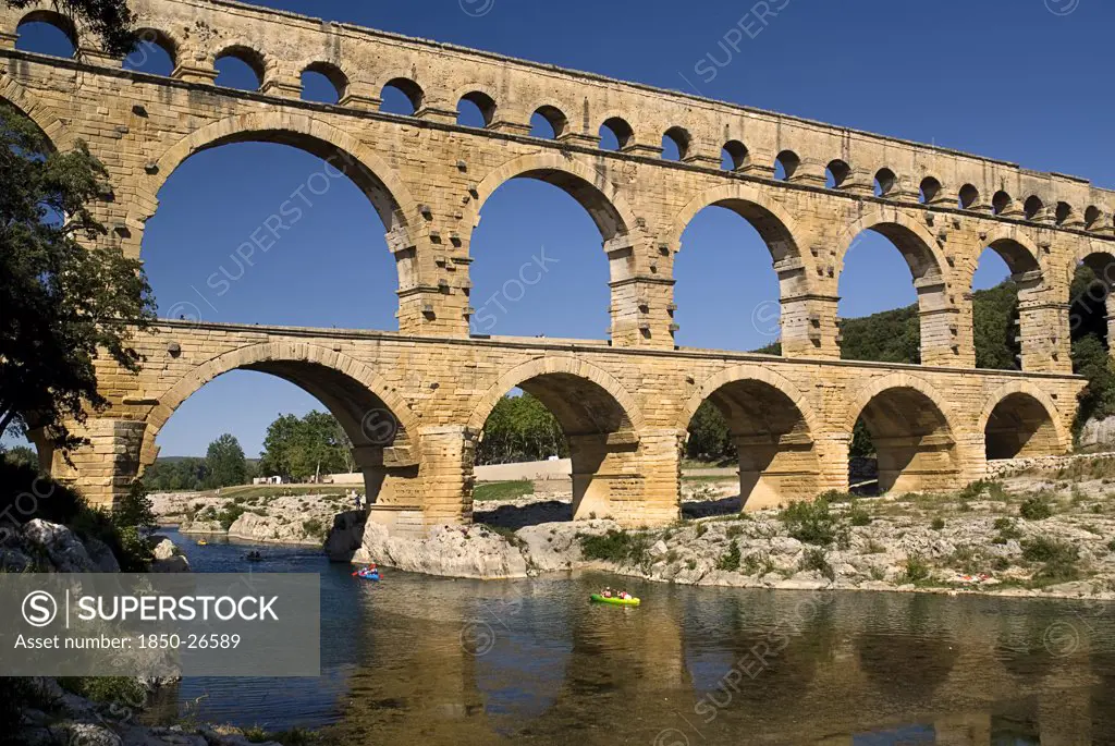 France, Provence Cote DAzur, Gard, Pont Du Gard.  View From West Side Of The Roman Aqueduct In Glowing Evening Light With Passing Canoe And Reflection In The Water Below.