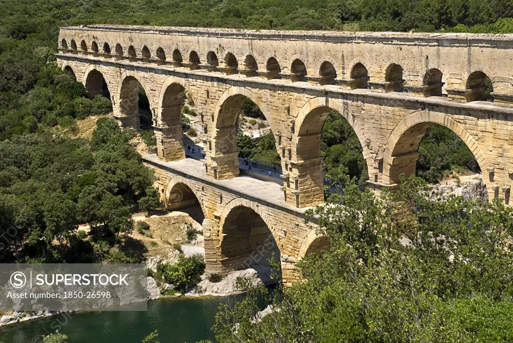 France, Provence Cote DAzur, Gard, Pont Du Gard Roman Aqueduct From A High Vantage Point On The Western Side Showing Three Tiers Of Continuous Arches Spanning River And Visitors On Bridge.