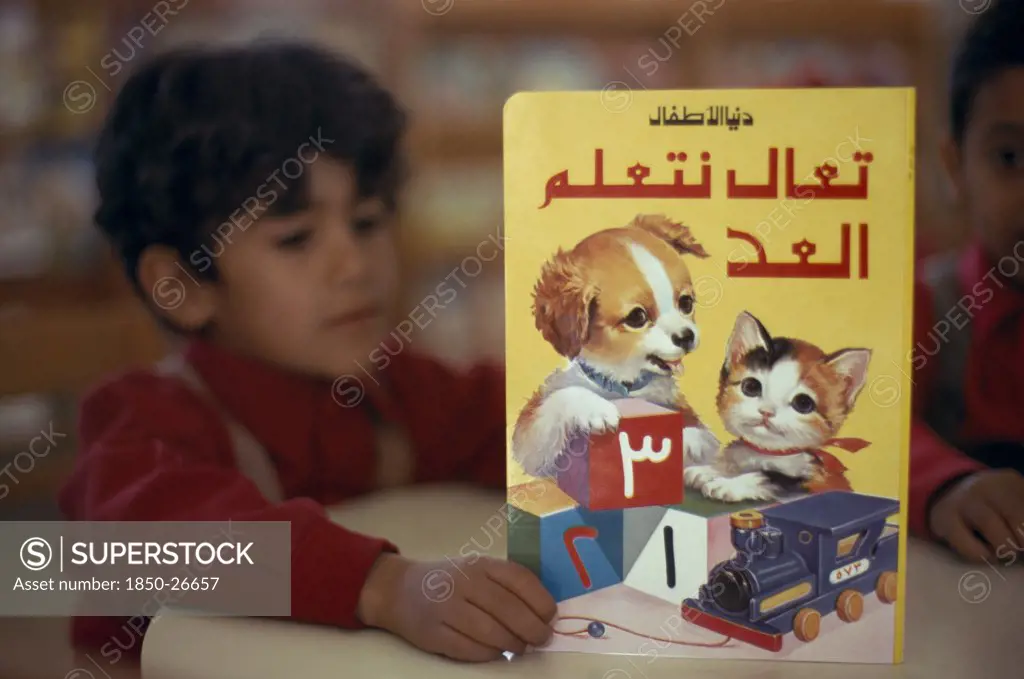 Kuwait, Education, School Boy Reading A Colourful Book Illustrated With A Kitten And Puppy