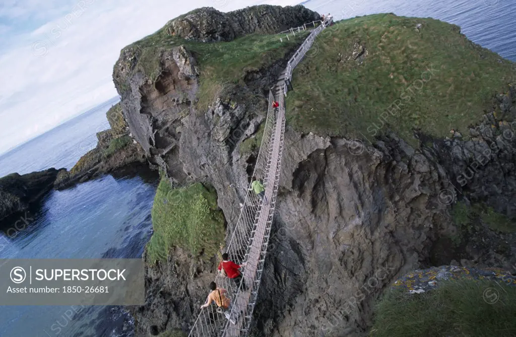 Northern Ireland, County Antrim, Ballintoy, Carrick-A-Rede Rope Bridge. Vistors Walking Over Rope Bridge Linking A Rocky Island To Cliffs.