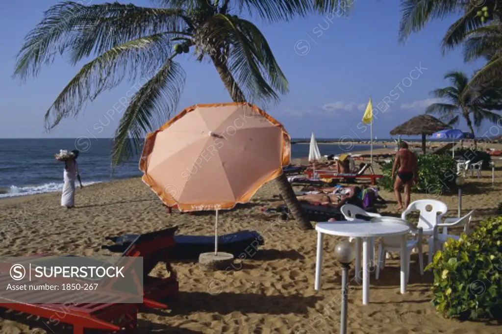 Sri Lanka, Negombo, Sandy Beach With Umbrella Shading Tourists Lying On Sunbeds And A Shell Vendor Dressed In White