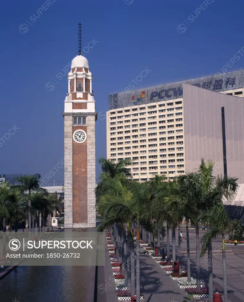China, Hong Kong, Kowloon, Kowloon Star Ferry Clock Tower At End Of Rectangular Pool Lined By Palms And Flowerbeds.