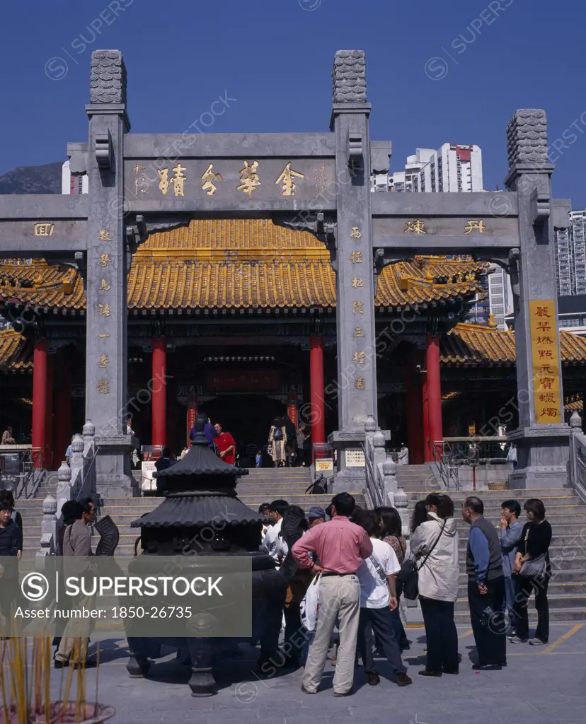 China, Hong Kong, Kowloon, Wong Tai Sin Taoist Temple Established In 1921.  Visitors Gathered Beside Incense Burner At Foot Of Flight Of Steps To Entrance Built In Traditional Chinese Style With Red Interior Pillars And Pagoda Style Roof.