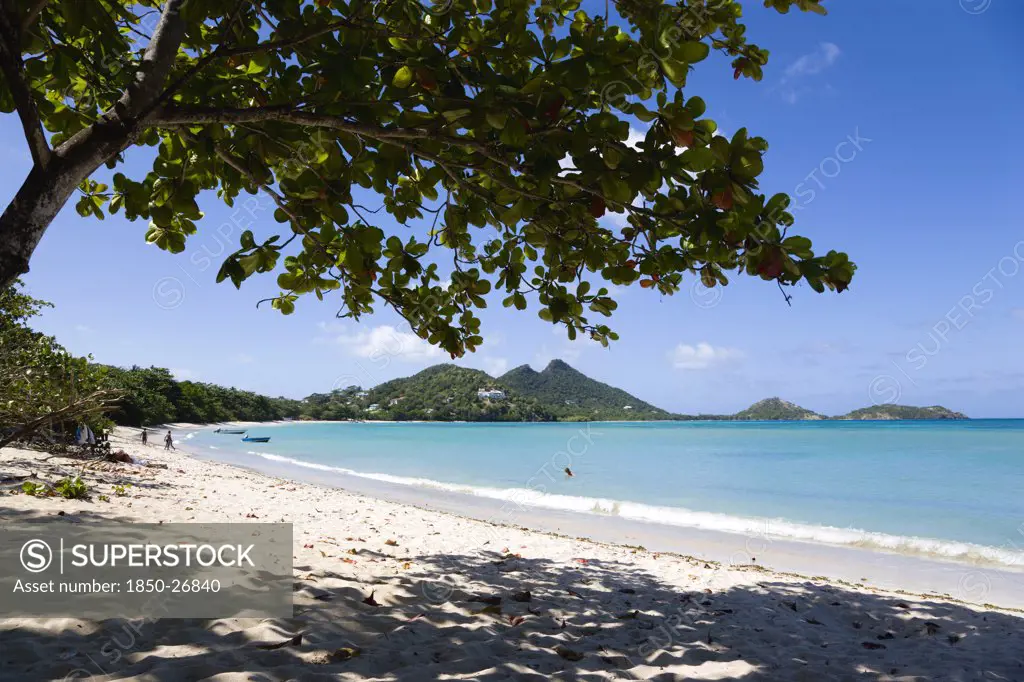West Indies, Grenada, Carriacou, The Calm Clear Blue Water Breaking On Paradise Beach In L'Esterre Bay With Cistern Point And The Sisiter Rocks In The Distance. A Small Number Of People On The Beach And In The Water