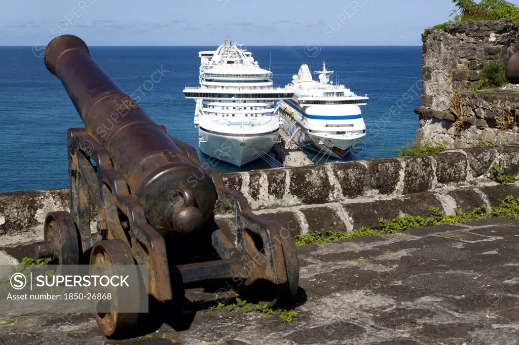 West Indies, Grenada, St George, An Old Canon Pointing Out To Sea At Fort George With Two Cruise Ships The Caribbean Princess And The Aida Aura Moored Below At The Cruise Ship Terminal In The Capital City Of St George'S With Passengers Walking On The Jetty Between The Two Liners
