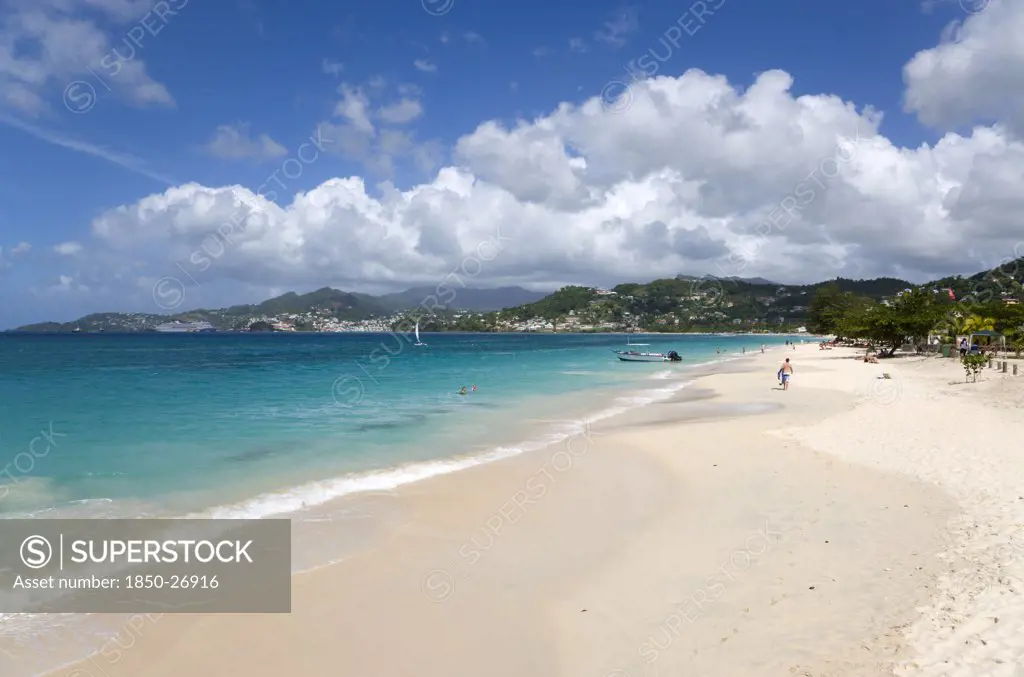 West Indies, Grenada, St George, Waves Of The Aquamarine Sea Breaking On The Two Mile Stretch Of Grand Anse Beach With People On The White Sandy Beach And The Capital City Of St George'S In The Distance