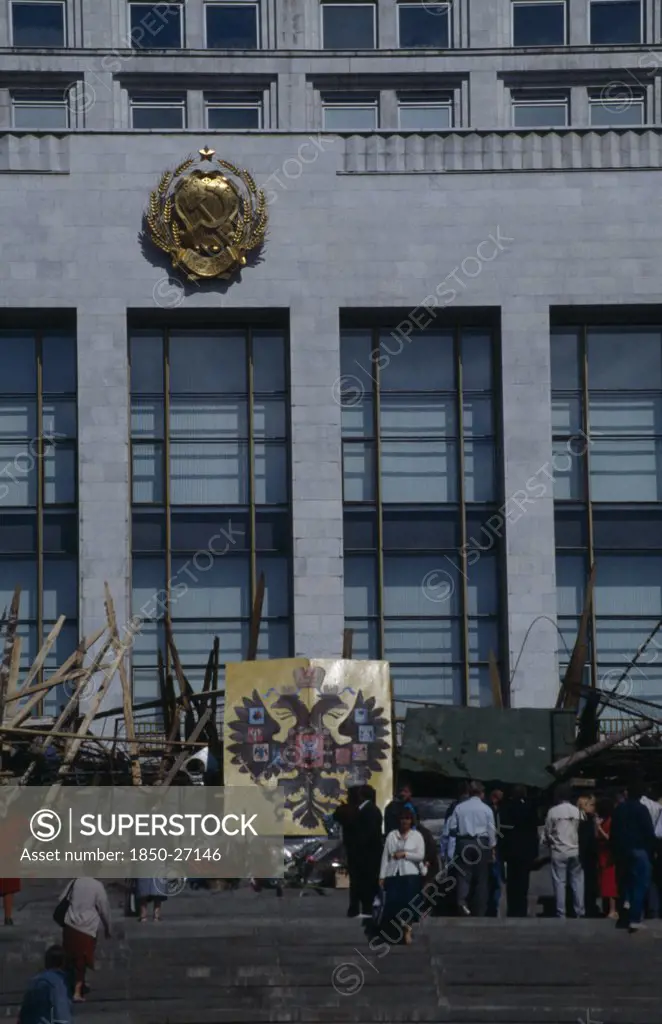 Russia, Moscow, Parliament Building With Barricades Made From Pieces Of Wood And Metal After An Attempted Coup. People Standing On The Steps Next To The Coat Of Arms Of The Russian Federation Emblem Which Depicts A Double Headed Eagle.