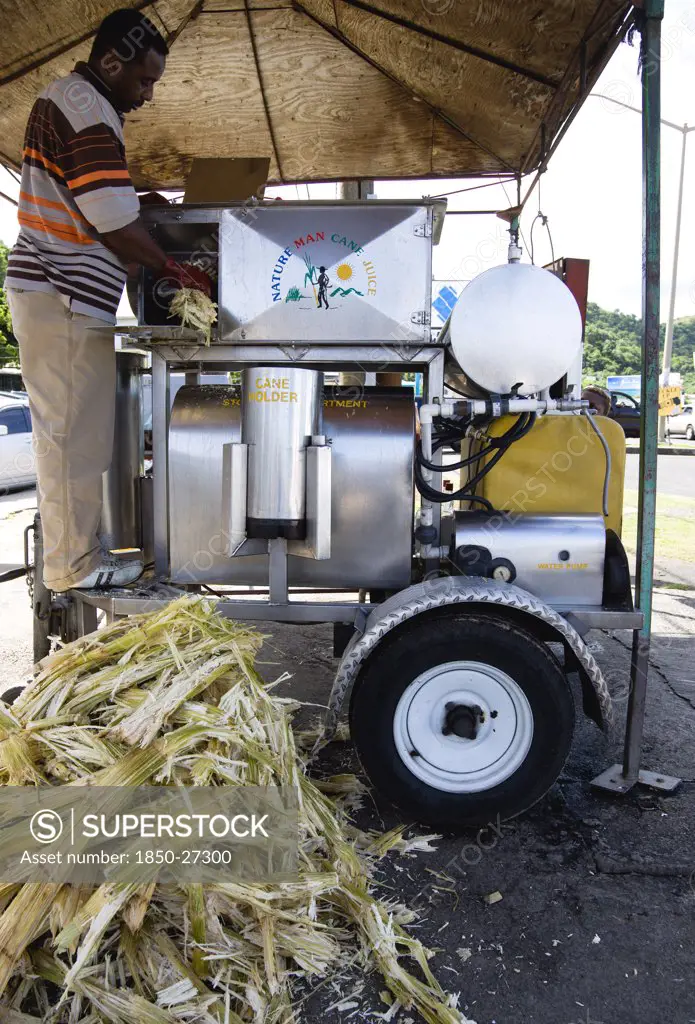 West Indies, Grenada, St George, Man Feeding Sugar Cane Into A Mobile Cane Juice Machine Beside Grand Anse Beach.
