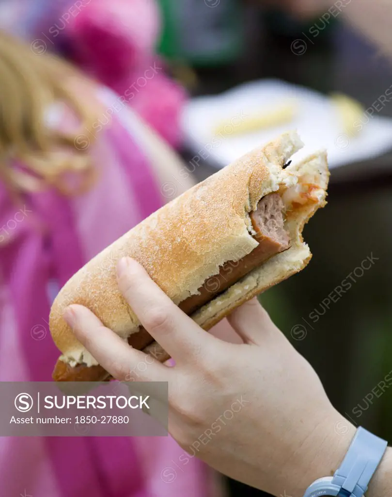 England, West Sussex, Findon, Findon Village Sheep Fair Teenage Girl Holding A Hot Dog With Tomato Ketchup And Onions With A Bite Taken Out Of It.