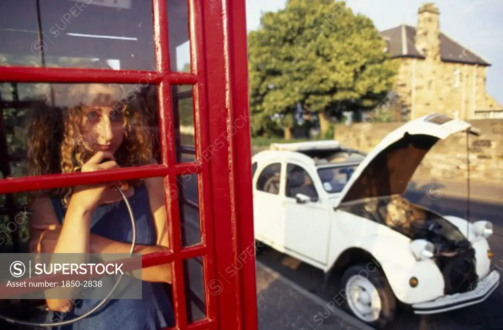 Communications, Telephone, Phone Box, Girl Making A Call In A Traditional Red Phone Box With Broken Down Citroen 2Cv Car Outside