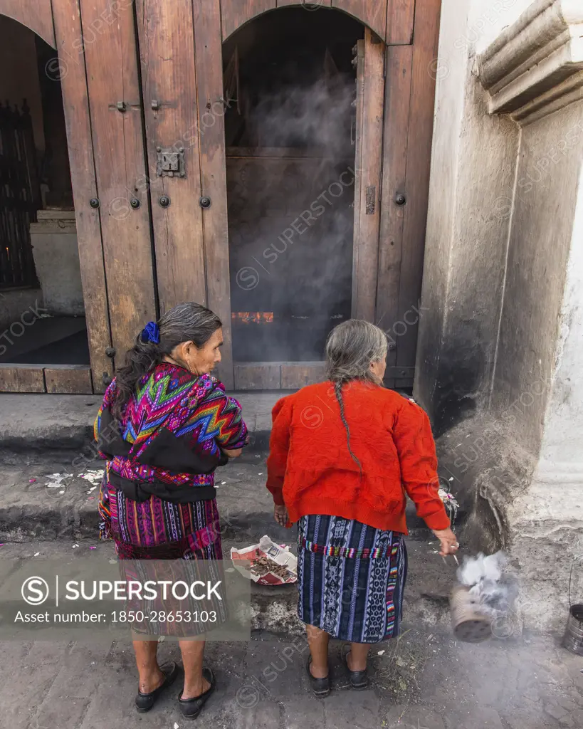 Guatemala, El Quiche Department, Chichicastenango, Two Quiche Mayan woman burn copal incense to the Mayan gods on the steps of the Church of Santo Tomas. They are swinging cans of smoking, burning resin.
