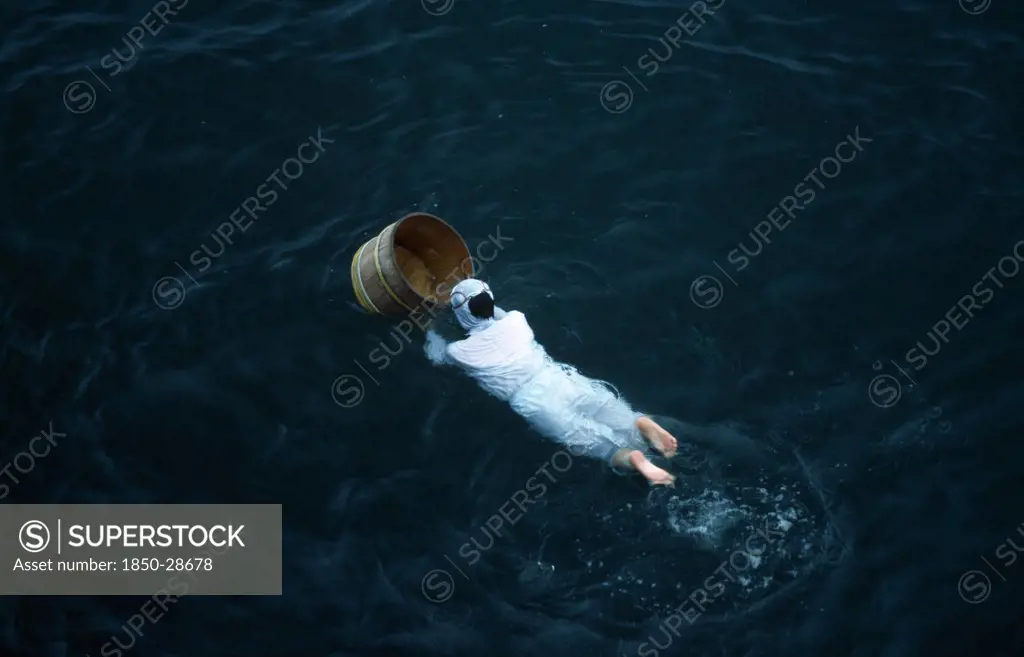 Japan, Honshu, Toba, Traditional Female Pearl Diver Swimming In The Water With Wooden Barrel For Collecting Oysters At The Mikimoto Pearl Farm In Mie Prefecture In Kansai Region.