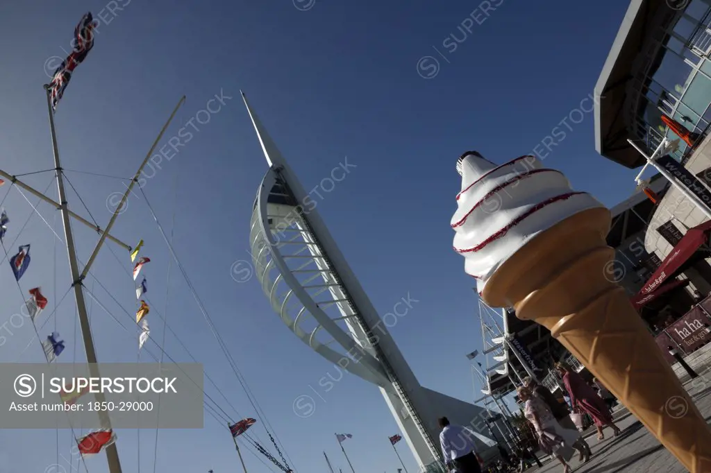 England, Hampshire, Portsmouth, Gun Wharf Quay. Spinnaker Tower And Boardwalk With Naval Flag Pole And Large Plastic Ice Cream Cone In The Foreground.