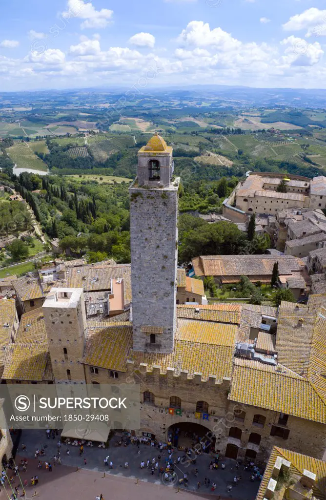 Italy, Tuscany, San Gimignano, View Of The Palazzo Vecchio Del Podesta Of 1239 With Its Medieval Tower With Tourists In The Piazza Del Duomo With Rooftops And Tuscan Farmland On The Slopes Of The Hill Town.