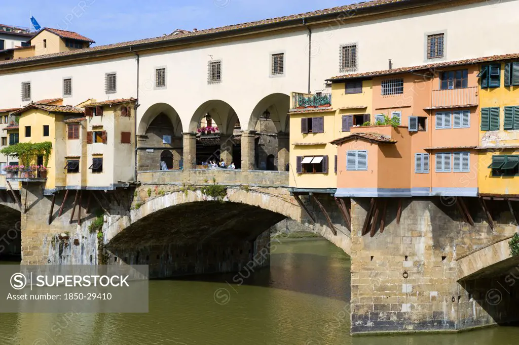 Italy, Tuscany, Florence, Ponte Vecchio Medieval Bridge Across River Arno With Sightseeing Tourists Beside Merchants Shops That Line Bridge And Hang Over The Water Below.