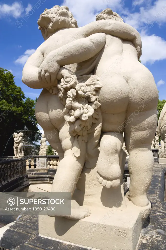 Germany, Saxony, Dresden, Statue Seen From Behind Of Two Fat Naked Figures Walking With Their Arms Around Each Other In The Restored Baroque Zwinger Palace Gardens.