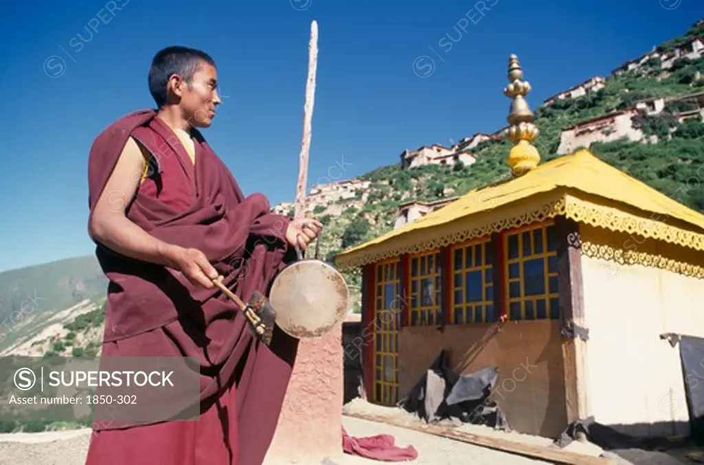 China, Tibet, Drigung Til Monastery, Monk Calling Other Monks To Prayer With A Drum.