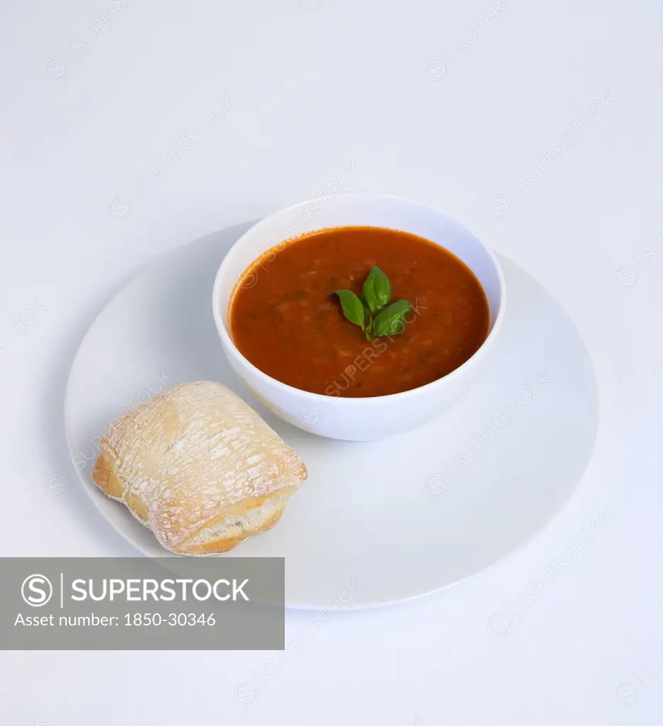 Food, Cooked, Soup, Bowl Of Tomato And Basil Soup On A Plate With A Rustic Bread Roll On A White Background.
